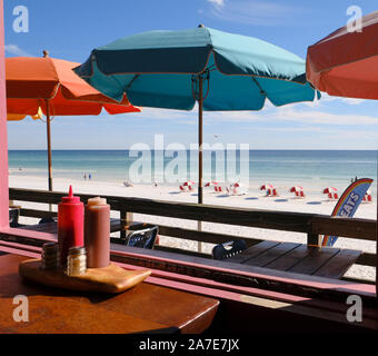 Table de restaurant à la plage de sable blanc à l'extérieur et des tables avec parasols colorés Pompano Joe's restaurant de fruits de mer à Miramar Beach FL. Banque D'Images
