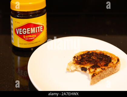 Sydney, Australie - Novembre 2, 2019 - Vegemite et beurre sur toast au levain avec morsure avec Vegemite jar dans l'arrière-plan. Une icône classique Banque D'Images