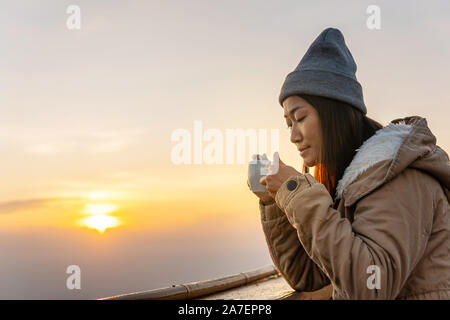 Une femme asiatique se trouve le café au lever du soleil sur le sommet d'une montagne. Banque D'Images