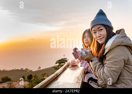 Femme asiatique deux café se trouve au lever du soleil sur le sommet d'une montagne. Banque D'Images