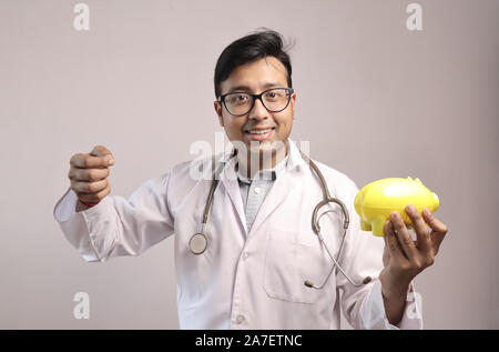 Femme médecin indien en blouse blanche et stéthoscope avec une tirelire jaune montrant des signes d'argent Banque D'Images