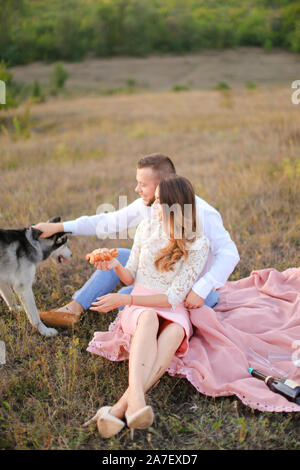 Jeune femme souriante et garçon assis sur l'herbe et jouer avec Husky. Banque D'Images