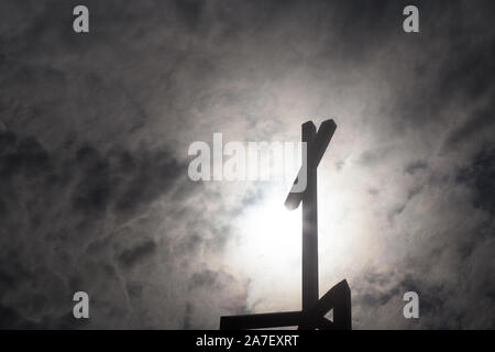 Un crucifix chrétien au sommet d'une église silhouetée par des rayons de lumière d'en haut. Banque D'Images