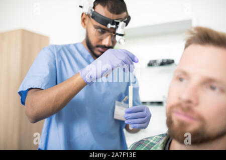 Jeune médecin sérieux dans les gants médicaux mettre stick dans la fiole avant traitement Banque D'Images