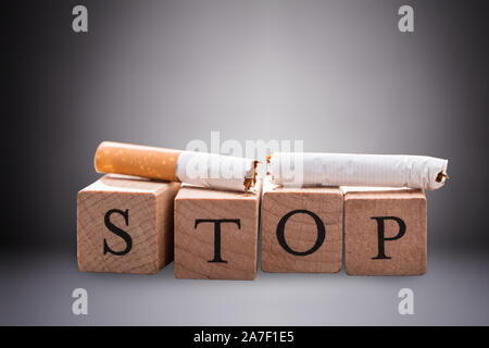 Close-up of Broken cigarette sur le bloc de bois d'arrêt contre l'arrière-plan gris Banque D'Images