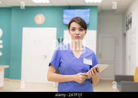 Clinicien confiant en uniforme, debout devant l'appareil photo lors de l'utilisation de touchpad Banque D'Images