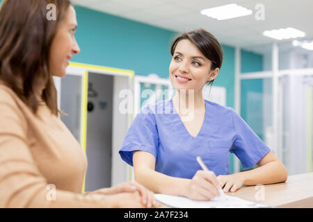 Médecin en uniforme souriant à tout patient consulting jeune femme dans les cliniques Banque D'Images