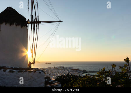 Jeune homme en short debout sur le bord près de moulin témoins de coucher du soleil à Mykonos , Grèce Banque D'Images