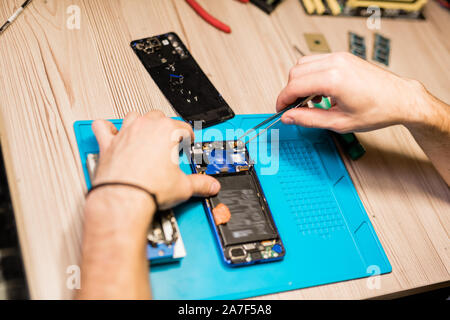 Mains de réparateur sur broken gadget à l'aide de brucelles pour fixer les pièces minuscules ou des boulons Banque D'Images