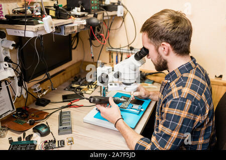 Outil manuel électrique avec l'homme à la microscope en pendant le travail avec les petits détails Banque D'Images