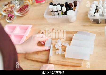 Mains de femme blanche de couper la masse de savon sur planche de bois par table Banque D'Images