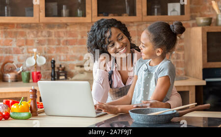 Maman et sa fille enlacés, lecture fiche sur ordinateur portable à la cuisine Banque D'Images