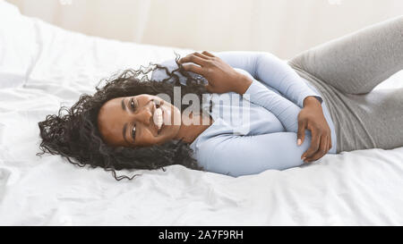 Jeune noir émotionnel girl enjoying matin au lit, serrant elle-même Banque D'Images