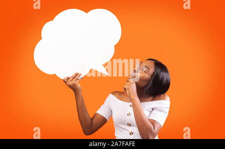 Jeune femme noire Holding Speech Bubble Debout, fond orange, immersive Banque D'Images