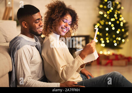 Heureux couple afro-américain don de Noël dans la salle de séjour, in front of Christmas Tree Banque D'Images