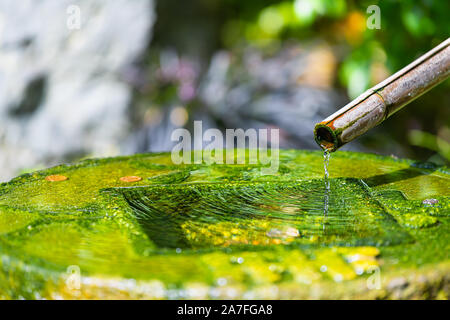 Fontaine à eau qui s'écoule à partir de bois de bambou tube dans stone rock à Kyoto bassin jardin japonais de Holland Park à Londres, au Royaume-Uni avec couleur vert mousse Banque D'Images