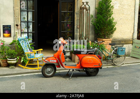 Scooter Orange stationné à l'extérieur du shopping à Monpazier, France avec vieux vélo et président Banque D'Images