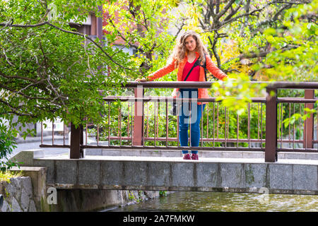 Quartier résidentiel de Kyoto au printemps avec femme sur le pont sur le canal de la rivière Takase en avril au Japon sur la journée ensoleillée avec des arbres verts Banque D'Images