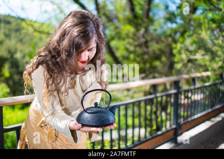 Jeune femme avec du thé théière traditionnelle par une clôture du luxe moderne piscine jardin de printemps dans la cour porche de la maison zen Banque D'Images