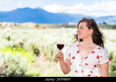 Dégustation de vin rouge femme en vue de Taos montagnes Sangre de Cristo de Ranchos de Taos valley en arrière-plan vignoble d'arrière-cour Banque D'Images