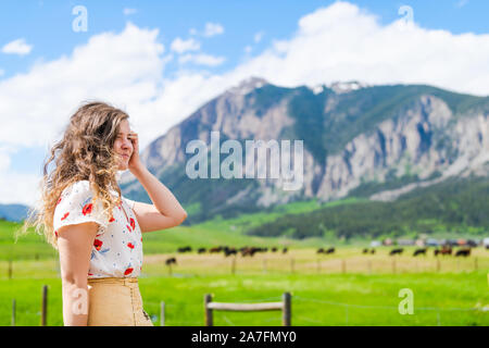 Crested Butte, Colorado avec happy young woman standing by fence et en été avec l'herbe verte et alpine sur la montagne aux beaux jours Banque D'Images