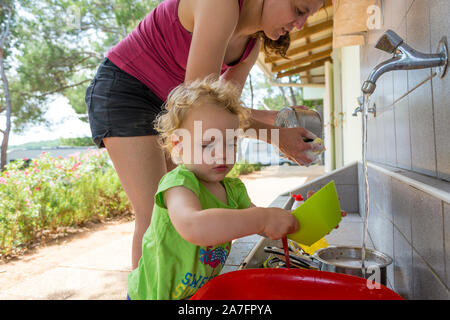 Fille aider sa mère à faire la vaisselle dans le camp de la mer. Banque D'Images