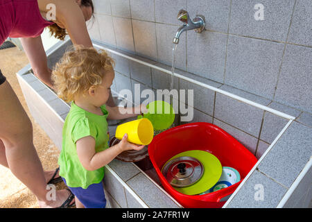 Fille aider sa mère à faire la vaisselle dans le camp de la mer. Banque D'Images