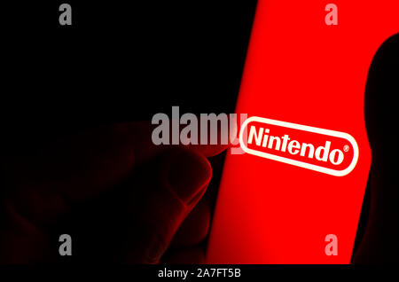 Logo Nintendo sur un écran de smartphone rouge dans une pièce sombre et un doigt de le toucher. Banque D'Images