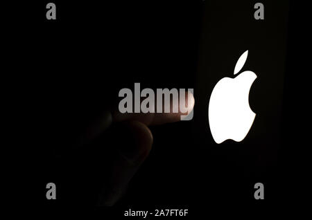 Logo Apple sur un écran de smartphone dans une pièce sombre et un doigt de le toucher. Banque D'Images