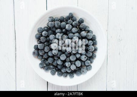 Plaque blanche avec petits fruits congelés aronie sur un tableau blanc en bois. Vue d'en haut. Banque D'Images