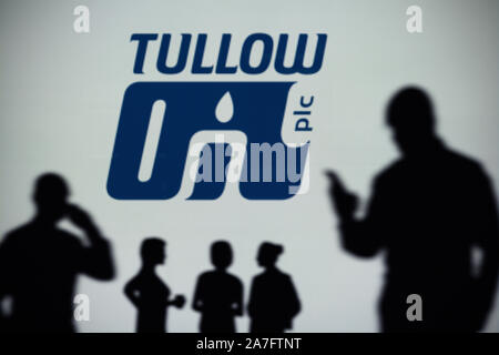 Le logo de Tullow Oil est vu sur un écran LED à l'arrière-plan tandis qu'une silhouette personne utilise un smartphone (usage éditorial uniquement) Banque D'Images