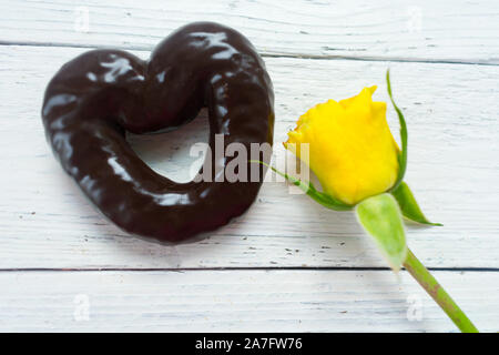 Cookies aux pépites de chocolat en forme de coeur et rose jaune sur un fond de bois blanc. Banque D'Images