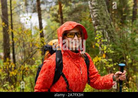 Smiling woman traveler avec un sac à dos de promenades à travers la forêt d'automne par temps de pluie Banque D'Images