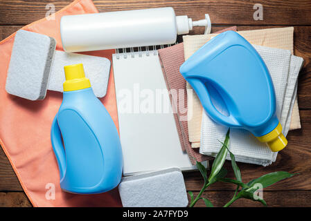 L'offre de lavage, adoucisseur, détergent, linges à vaisselle et le bloc-notes page blanche sur table en bois. Conseils à la personne des maquettes. Banque D'Images