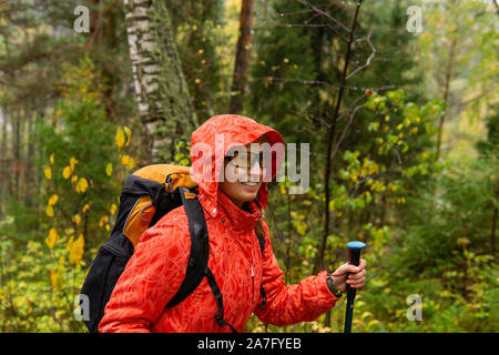 Smiling woman traveler avec un sac à dos de promenades à travers la forêt d'automne par temps de pluie Banque D'Images