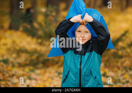 Petit garçon avec un sac poubelle gonflé sur sa tête dans une forêt à l'automne Banque D'Images