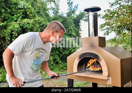 Man cooking pizza artisanale à l'extérieur dans un four au feu de bois Forno Bravo, fabriqué avec des ingrédients biologiques de Auberge Le Serendipity, In Browntown, Wisconsin, États-Unis Banque D'Images