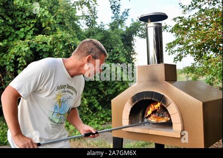 Man cooking pizza artisanale à l'extérieur dans un four au feu de bois Forno Bravo, fabriqué avec des ingrédients biologiques de Auberge Le Serendipity, In Browntown, Wisconsin, États-Unis Banque D'Images