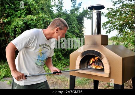 Man cooking pizza artisanale à l'extérieur dans un four au feu de bois Forno Bravo, fabriqué avec des ingrédients biologiques de Auberge Le Serendipity, In Browntown, Wisconsin, États-Unis Banque D'Images