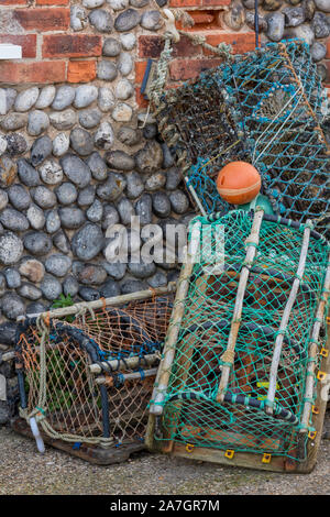 Articles de pêche et les engins de pêche abandonnés et le homard ou les casiers appuyé contre un mur de pierre de silex sur un quai de North Norfolk, au Royaume-Uni. Banque D'Images