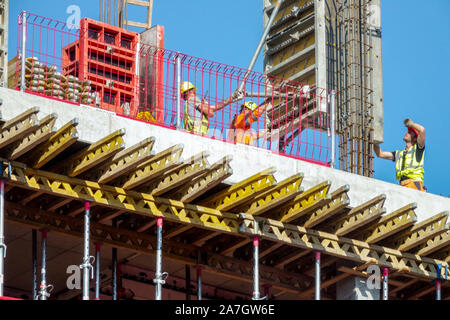 Trois travailleurs de la construction sont précisément régler le bloc de béton par grue Banque D'Images