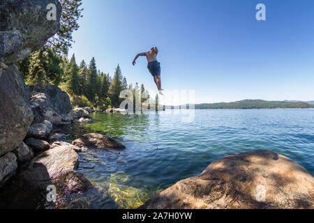 Jeune homme sautant d'une falaise rocheuse de la colline des bains à remous en à coeur d' Alene Lake dans le Nord de l'Idaho Banque D'Images