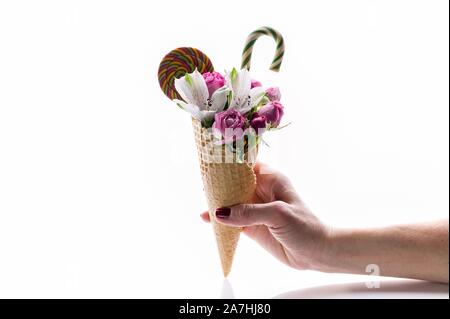 Main de femme élégante est titulaire d'un bouquet de fleurs avec des bonbons dans un cornet gaufré sur un fond blanc. Rose et alstrameria. Composition isolée Banque D'Images