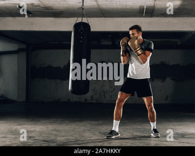 Muscle à l'aide d'un jeune boxeur sac de frappe dans une salle de sport. Boxer hitting punching bag de vitesse Banque D'Images