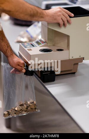 L'homme de remplir un sac en plastique avec des pièces métalliques après les compter sur une machine électronique Banque D'Images