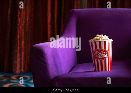 Papier à rayures seau de popcorn frais placé sur le doux Fauteuil violet vibrant au cours de showtime en cinéma Banque D'Images