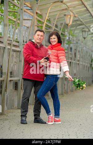 Couple avec un bouquet de fleurs et champagne. D'âge mûr avec un bouquet de fleurs. Banque D'Images