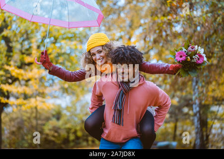 Homme noir portant son Caucasian girl s'y greffent en automne Banque D'Images