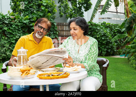 Senior couple reading newspaper ensemble et prendre le petit déjeuner dans la cour intérieure à la table de leur maison Banque D'Images