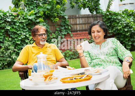 Smiling Couple âgé assis-sur-table ont un petit déjeuner boire le thé en-cour de leur maison à Banque D'Images